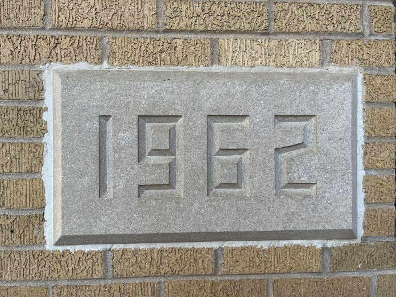 A gray stone plaque with the engraved number 1962 set into a tan brick wall.