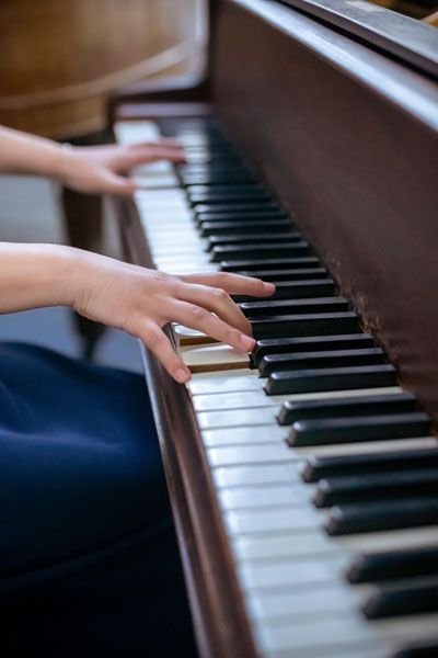 Close-up of hands playing the keys of a wooden upright piano.