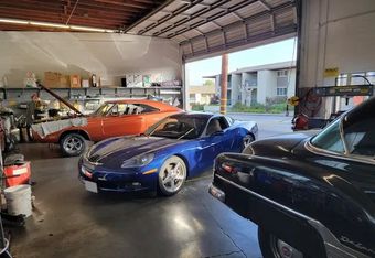 Sports cars parked inside a garage, blue convertible, black coupe, and orange classic car.