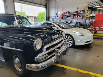 Classic black vintage car and white Tesla parked inside an auto workshop.