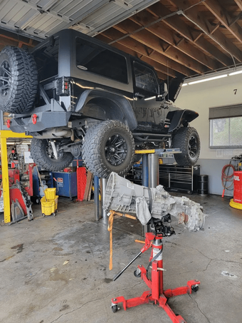 Black off-road truck lifted in a garage, with tools and equipment underneath it.