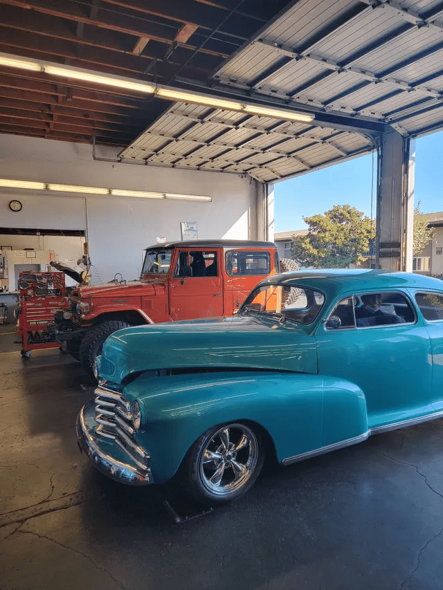 Classic cars in a garage: a turquoise coupe in front of an orange vintage truck.