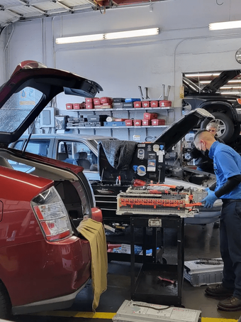 Red SUV with open trunk in auto repair shop; mechanic works on tools at a workbench.