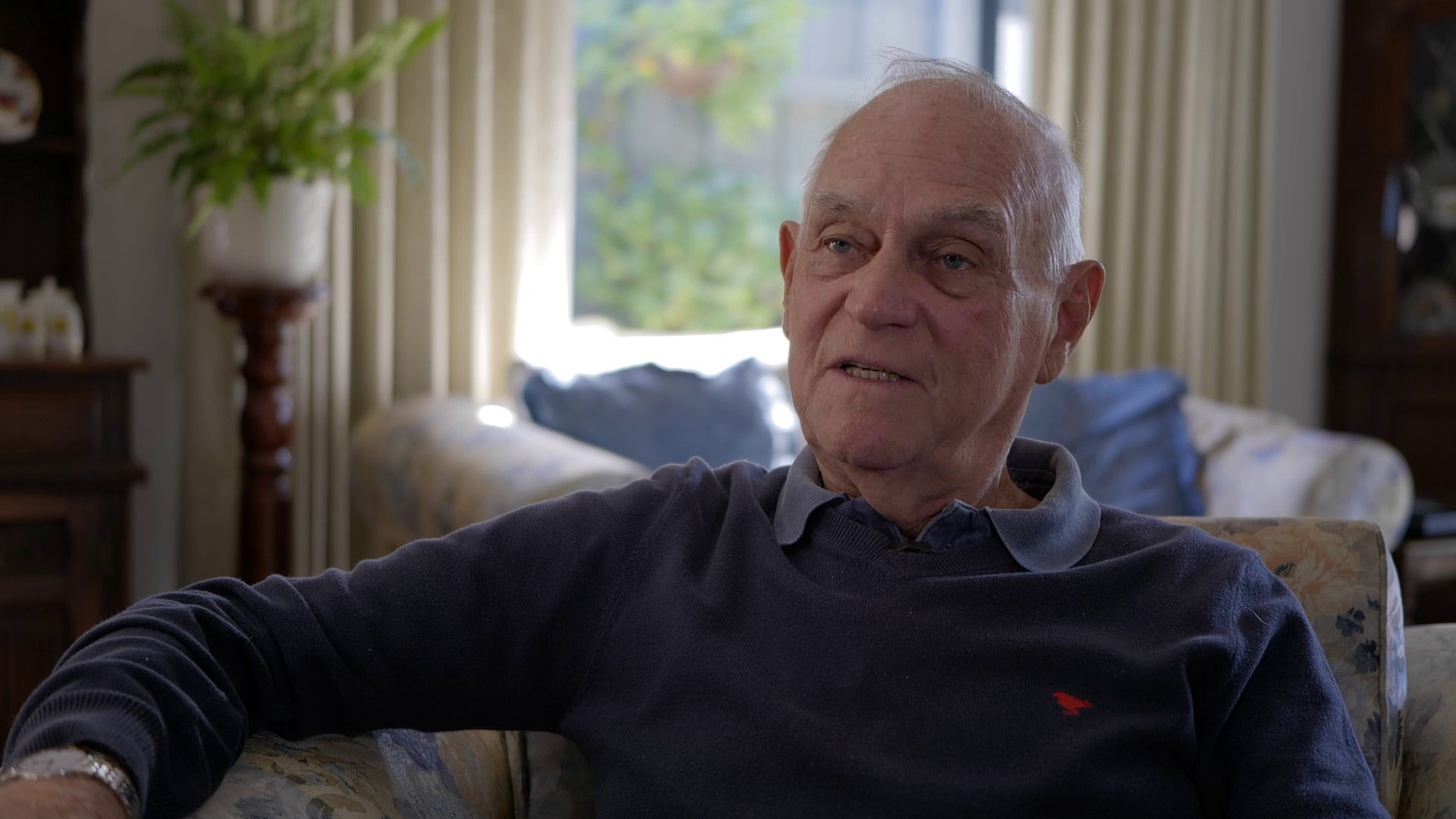 Mature man sitting on a couch being interviewed.