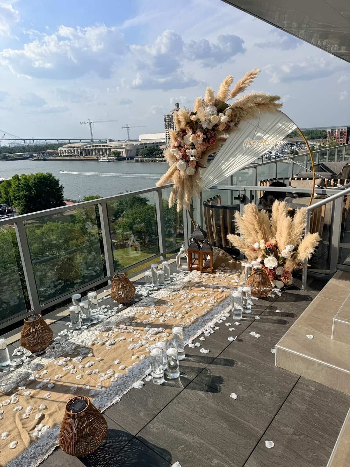 Outdoor waterfront wedding setup with white chairs, pampas grass arches, and a long decorated aisle under cloudy skies