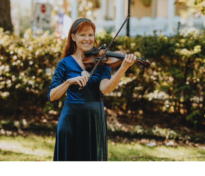 Woman in a blue dress playing violin outdoors in a sunny garden.
