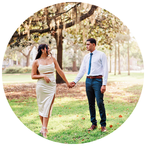 Couple holding hands in a sunlit park, with trees and grass around them
