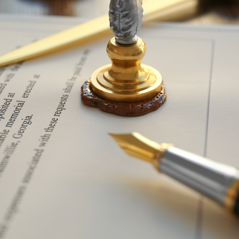 Gold pen and wax seal on a document, with text visible in the background