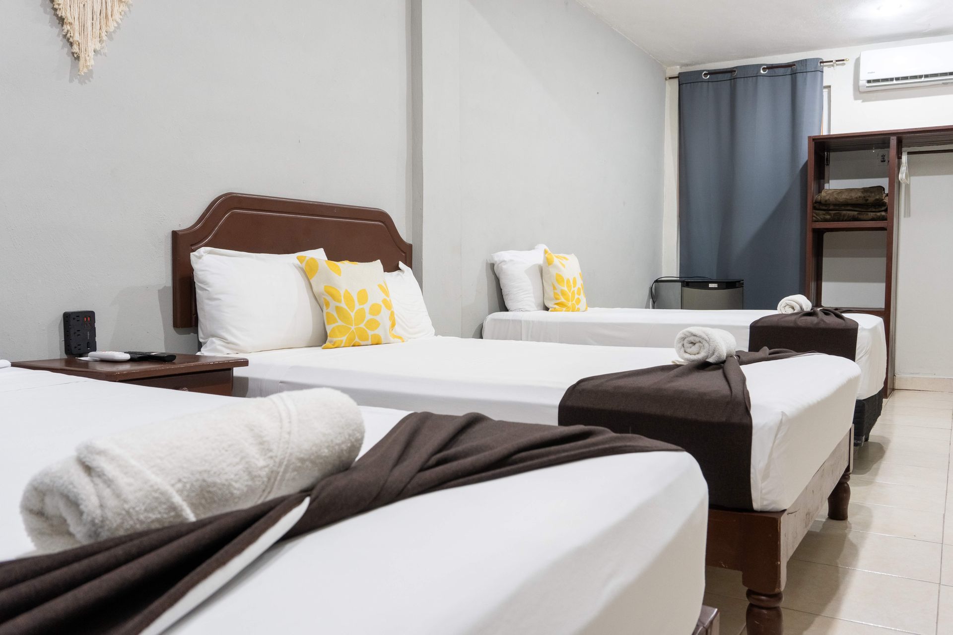 Dos camas individuales en habitación luminosa de hotel con sábanas blancas, cabeceros marrones y ventana con cortinas azules.