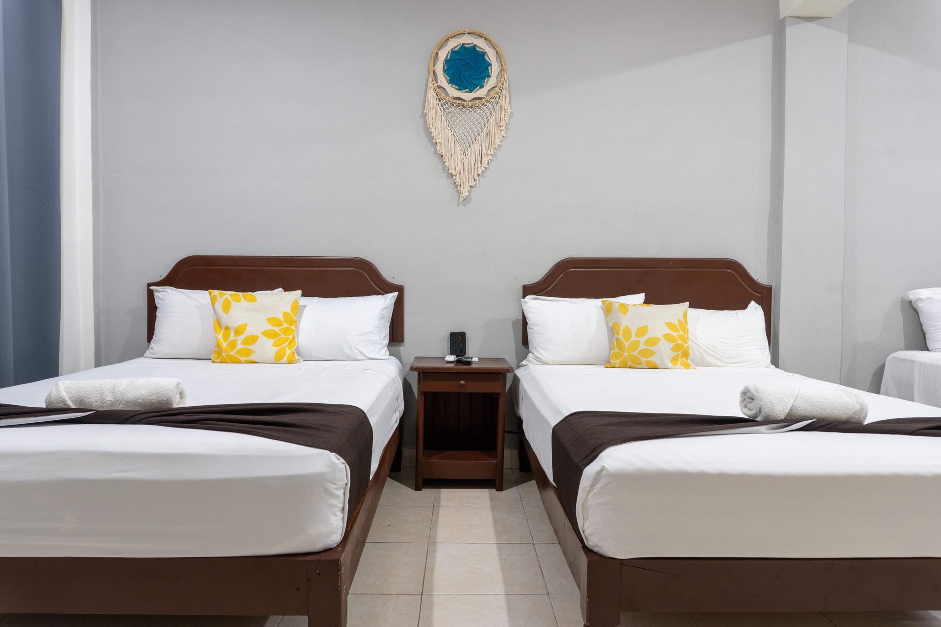 Dos camas individuales con sábanas blancas en habitación sencilla, con mesita de noche y decoración en la pared.