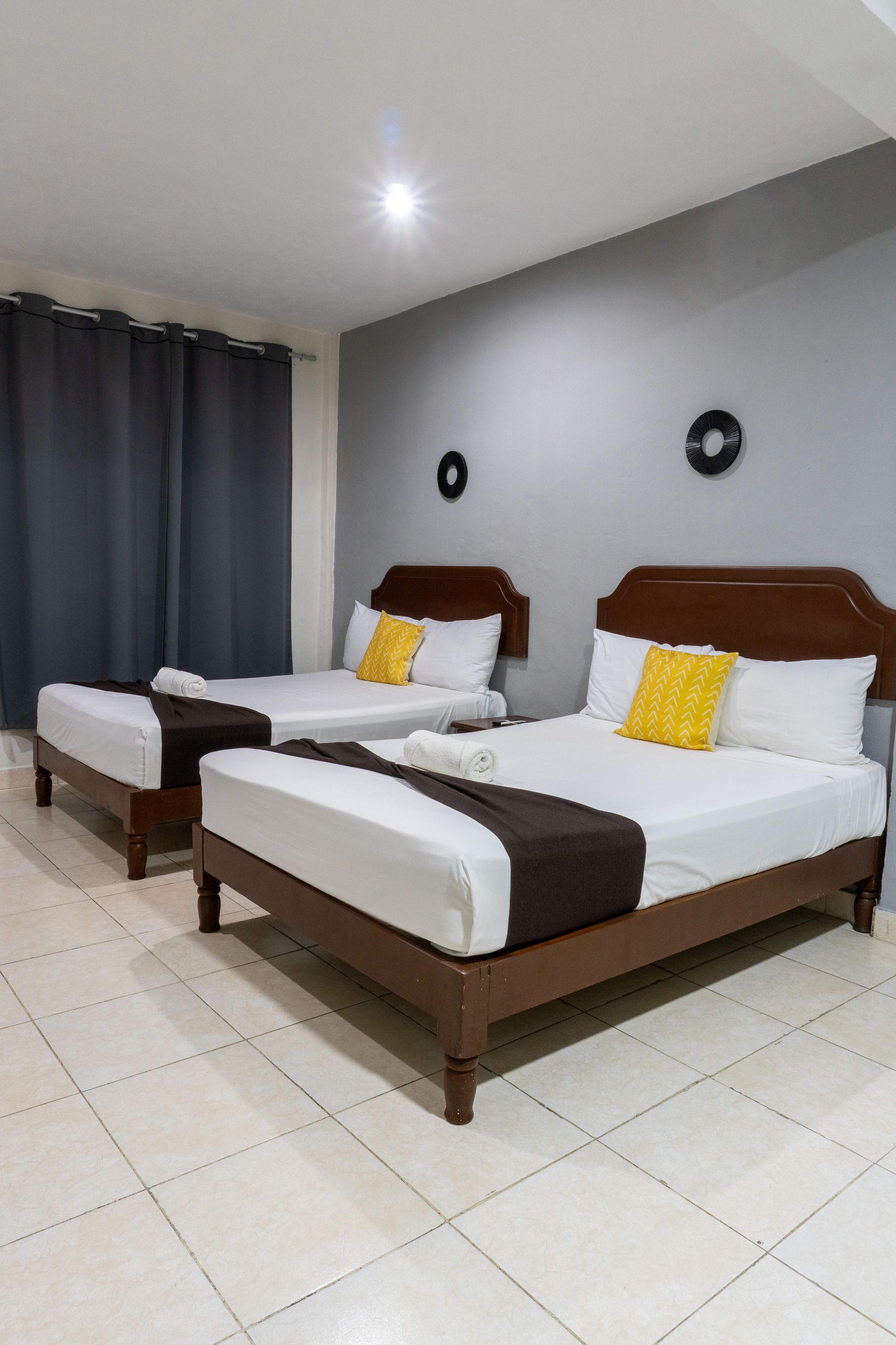 Habitación de hotel minimalista con dos camas individuales, ropa de cama blanca, cabeceros marrones y paredes grises.