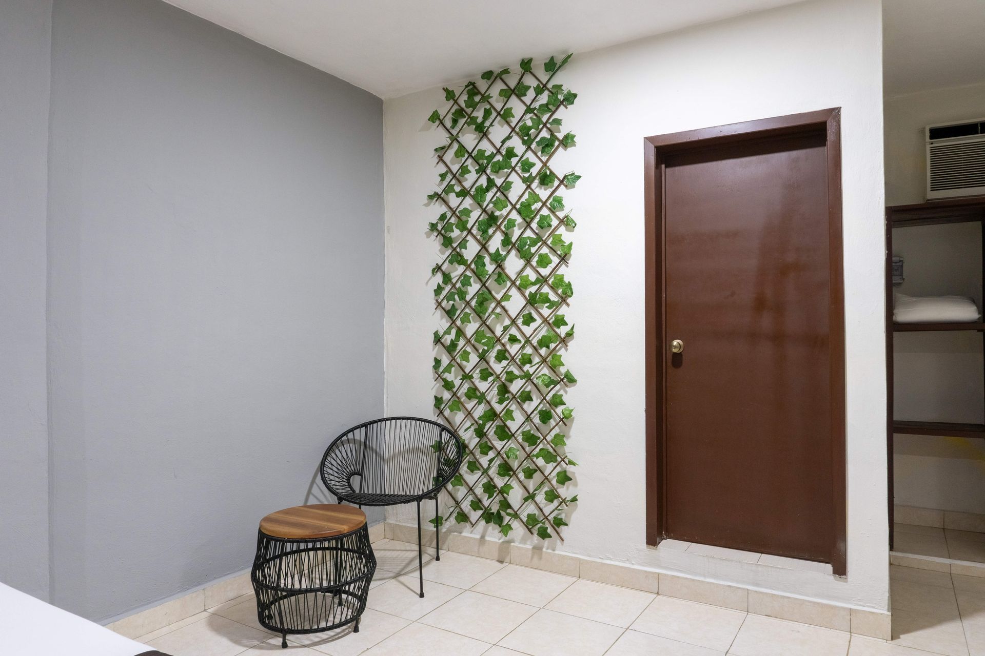 Pequeño patio con dos sillas, una puerta de madera y una celosía vertical verde sobre un suelo de baldosas claras.