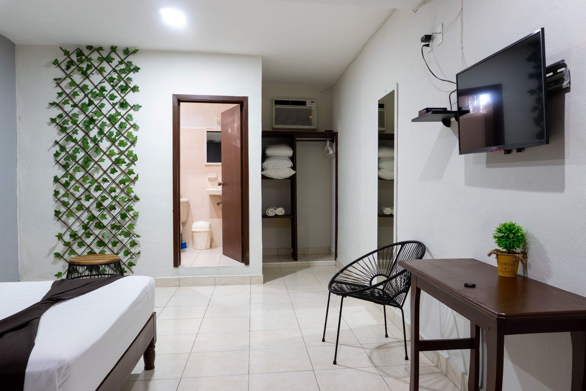Sala de estar moderna con televisor montado en la pared, mesa y silla pequeñas, puerta y decoración con plantas.
