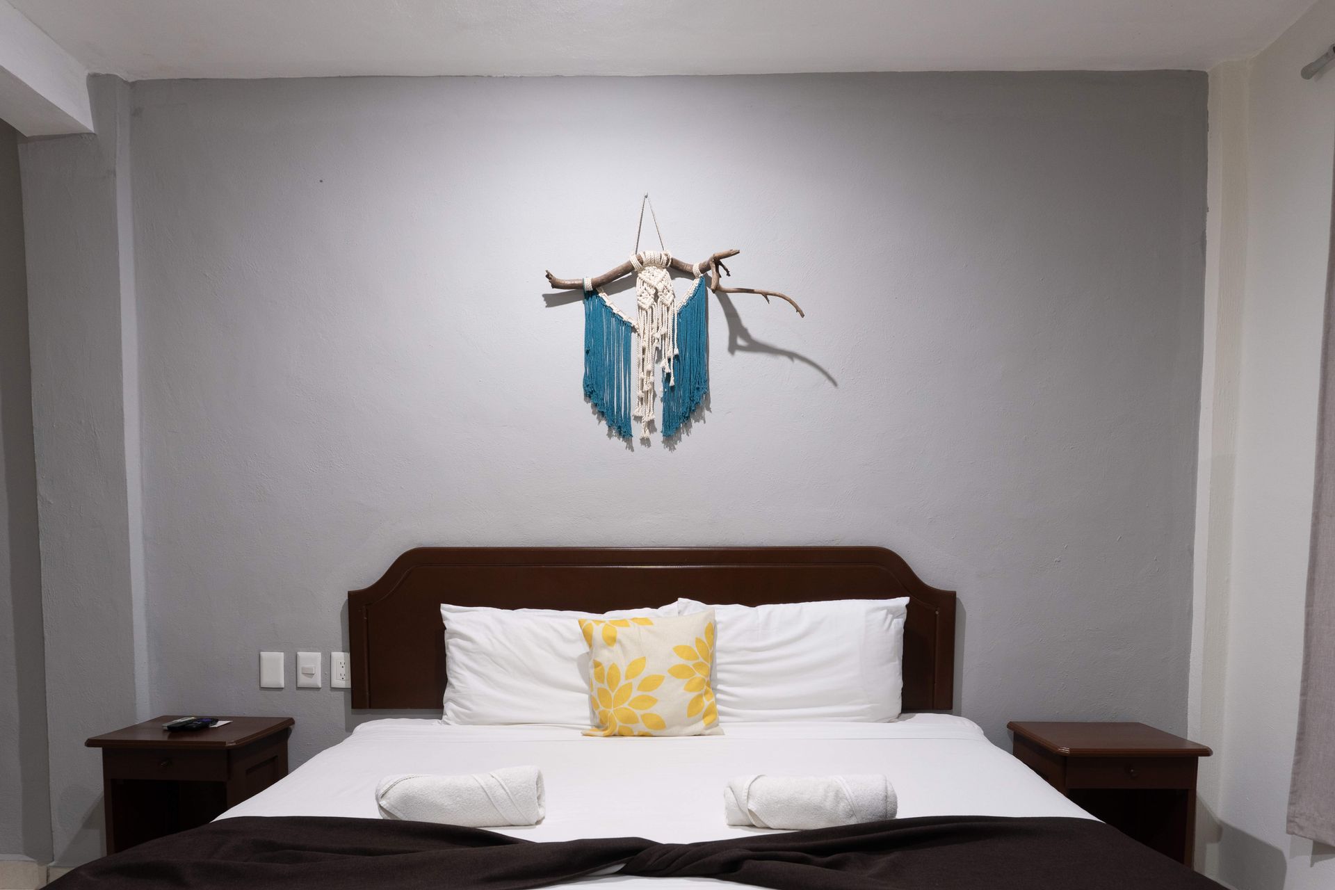 Dormitorio moderno con cama, almohadas blancas, paredes grises y cuadro azul sobre el cabecero.