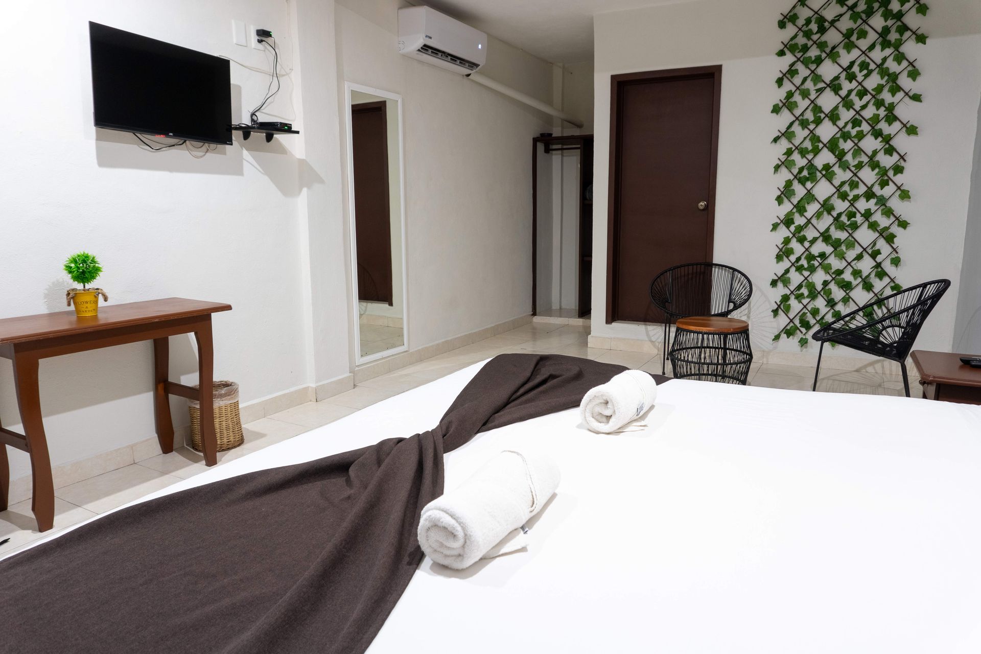 Habitación minimalista de hotel con cama, TV en pared, mesa pequeña, sillas y pared decorativa con diseño estampado.