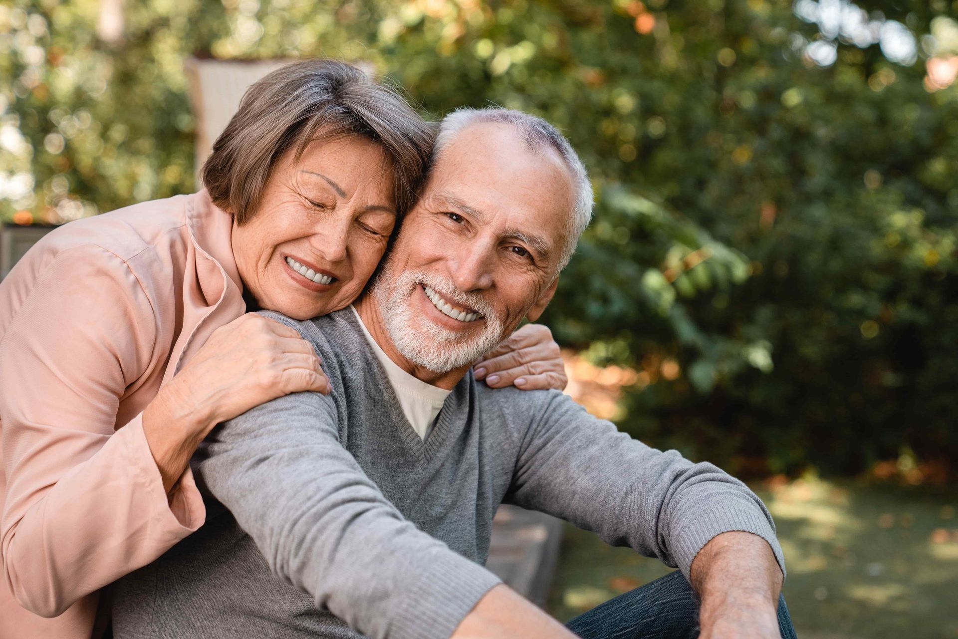 Two smiling people hugging outdoors in a sunlit park