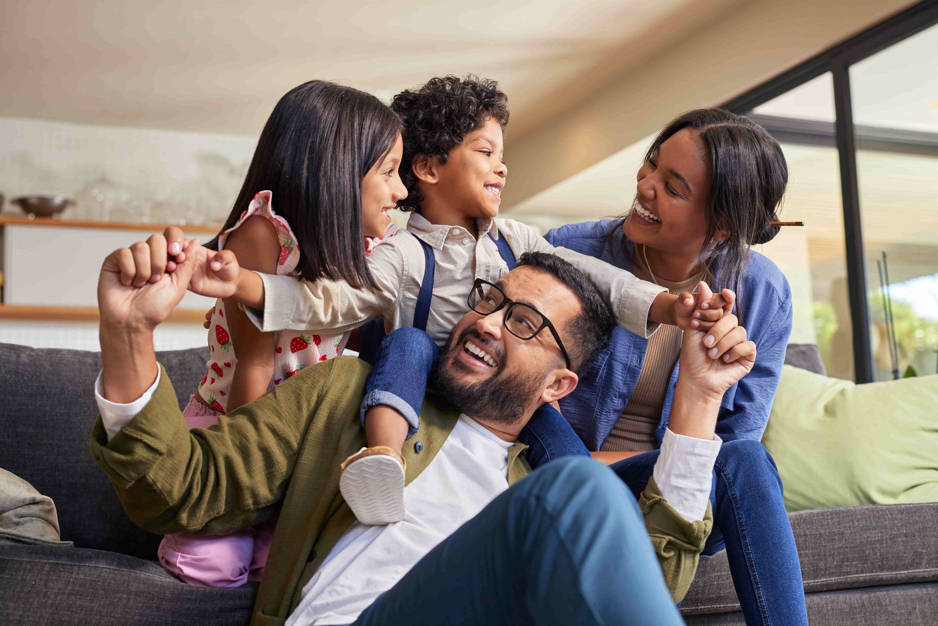 Family sitting together on a couch, smiling and playing with a child in a bright living room