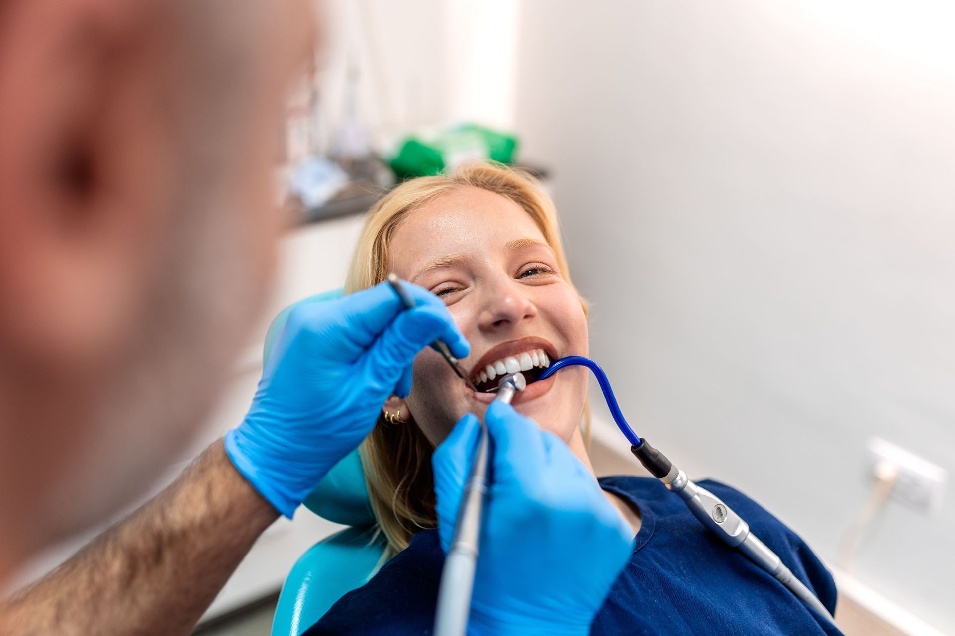 Dentist examining a smiling patient’s teeth with blue-gloved hands and dental tools