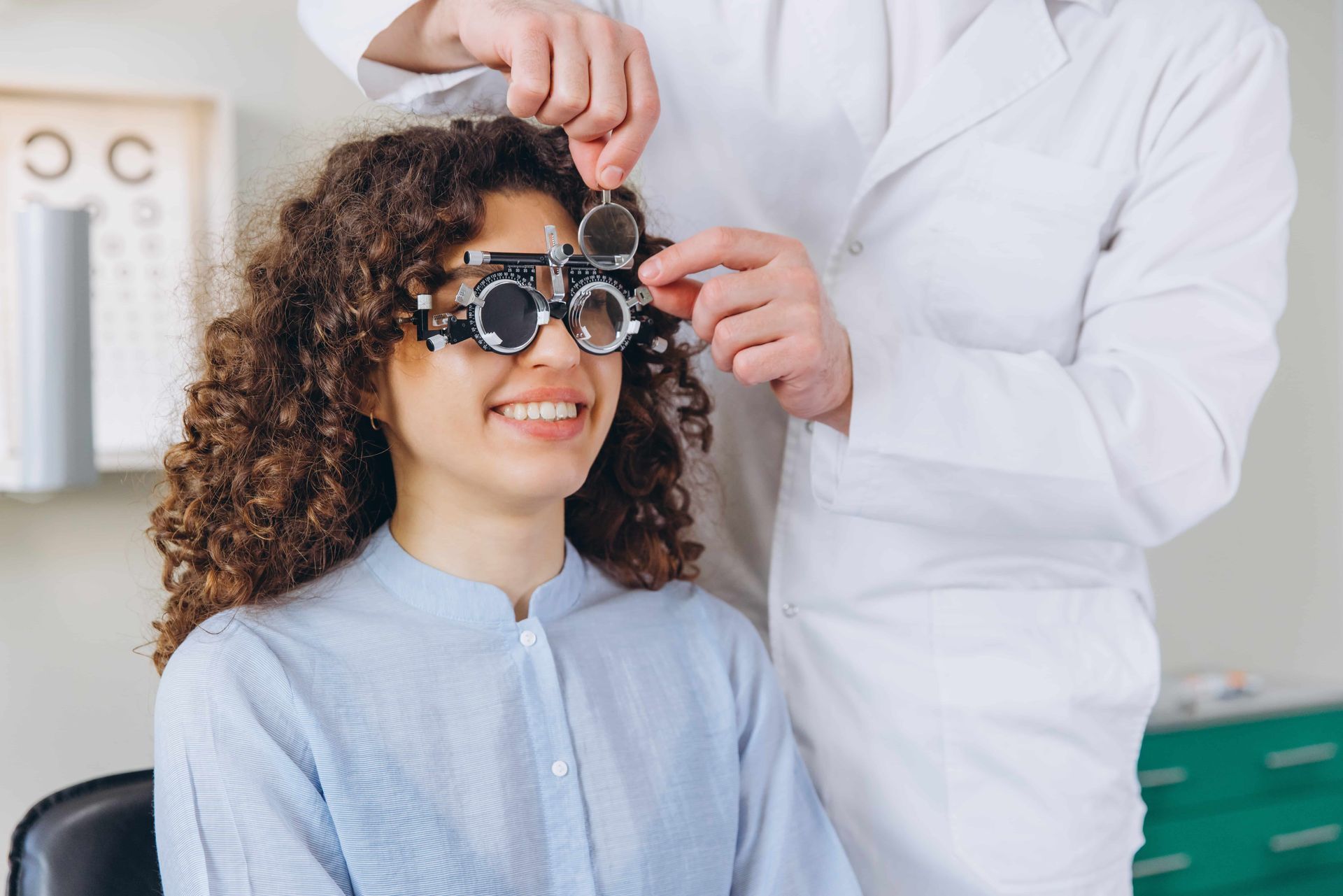 Optometrist adjusting glasses on a smiling patient in an eye exam room