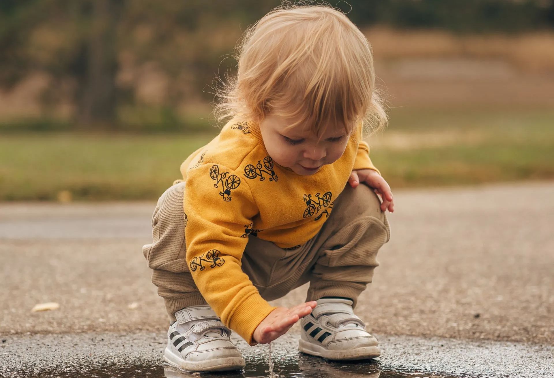 A baby is playing in a puddle on the side of the road.