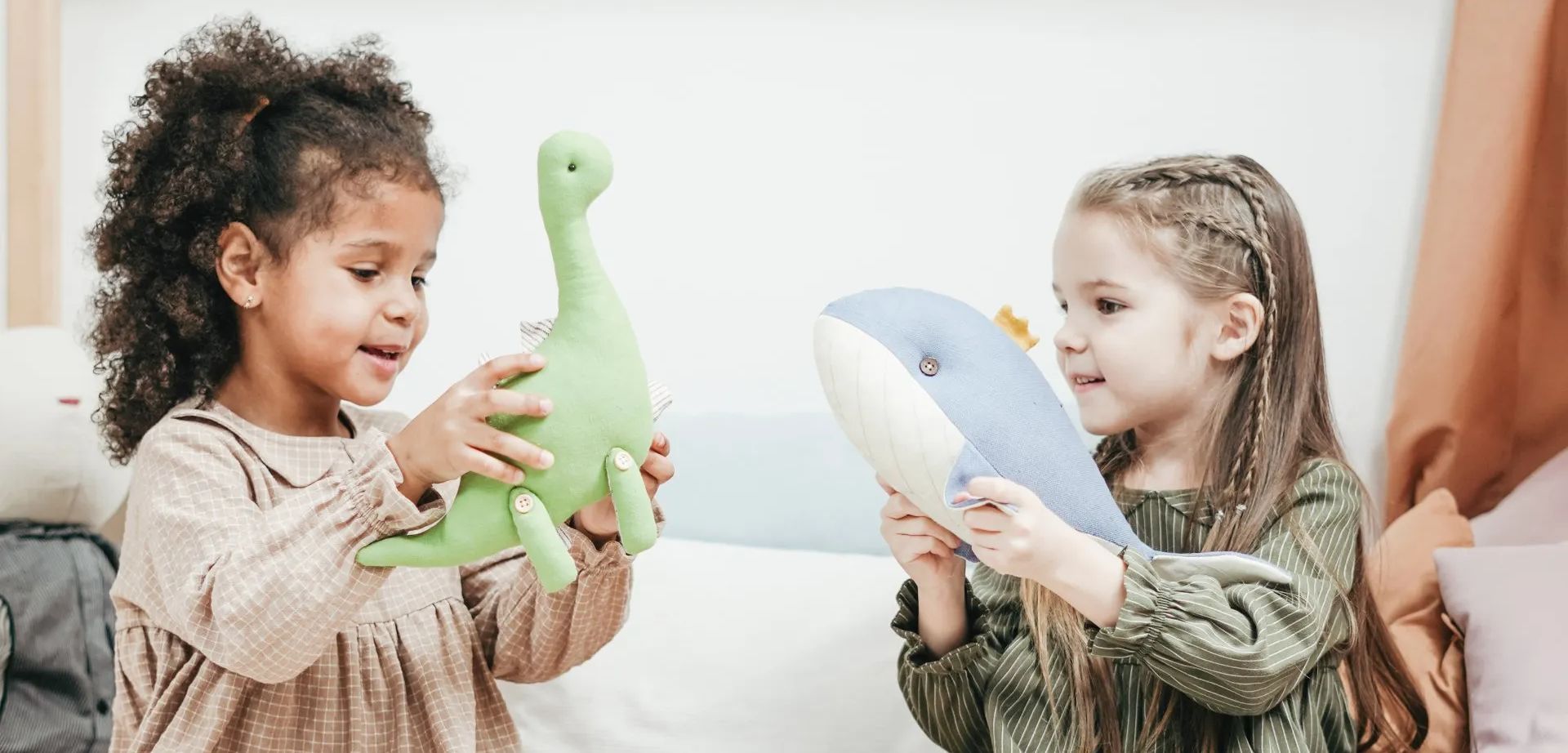 Two little girls are playing with stuffed animals on a bed.