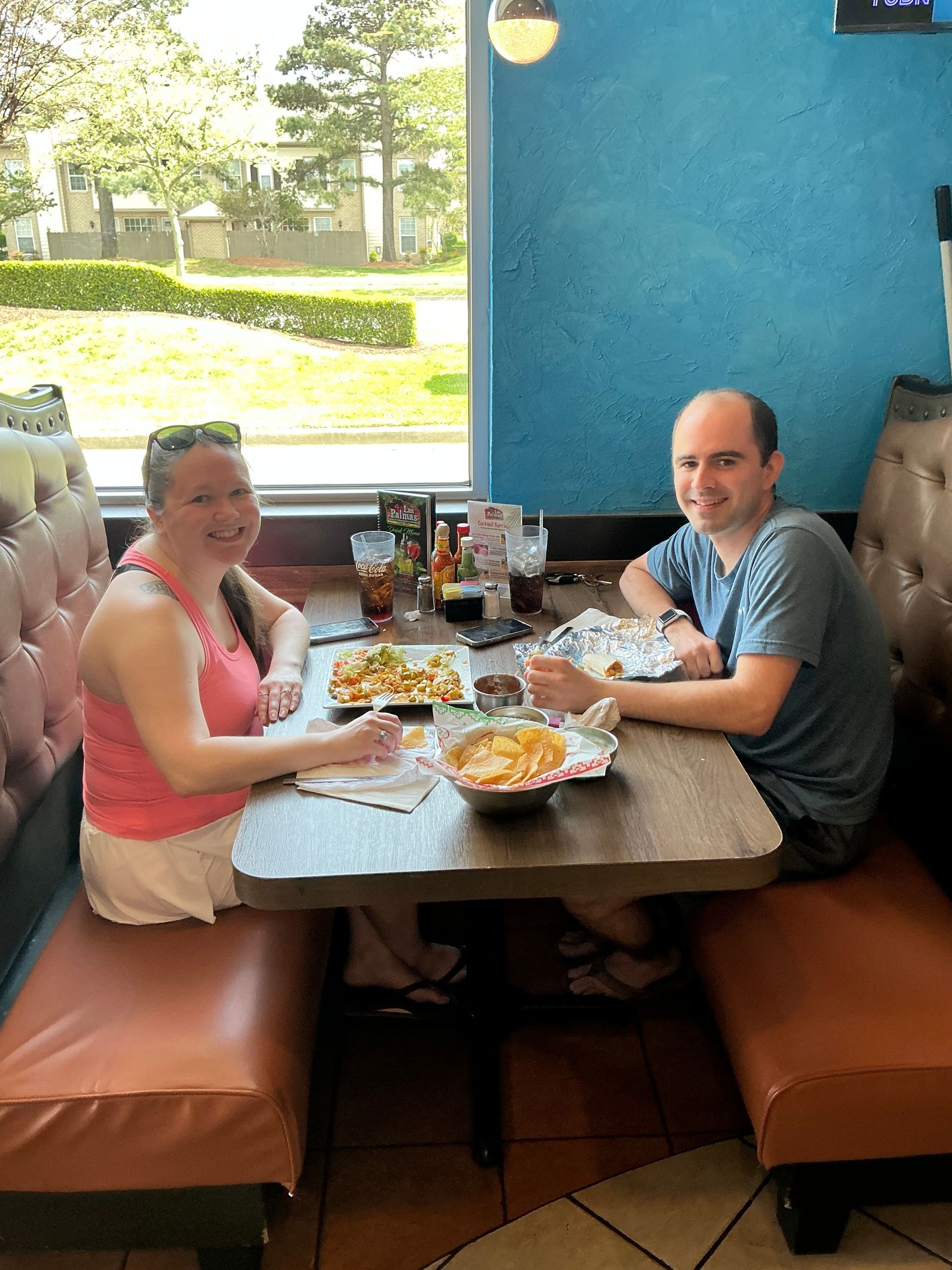 Two people seated at a booth in a restaurant eating. Bright and smiling, blue wall in background.
