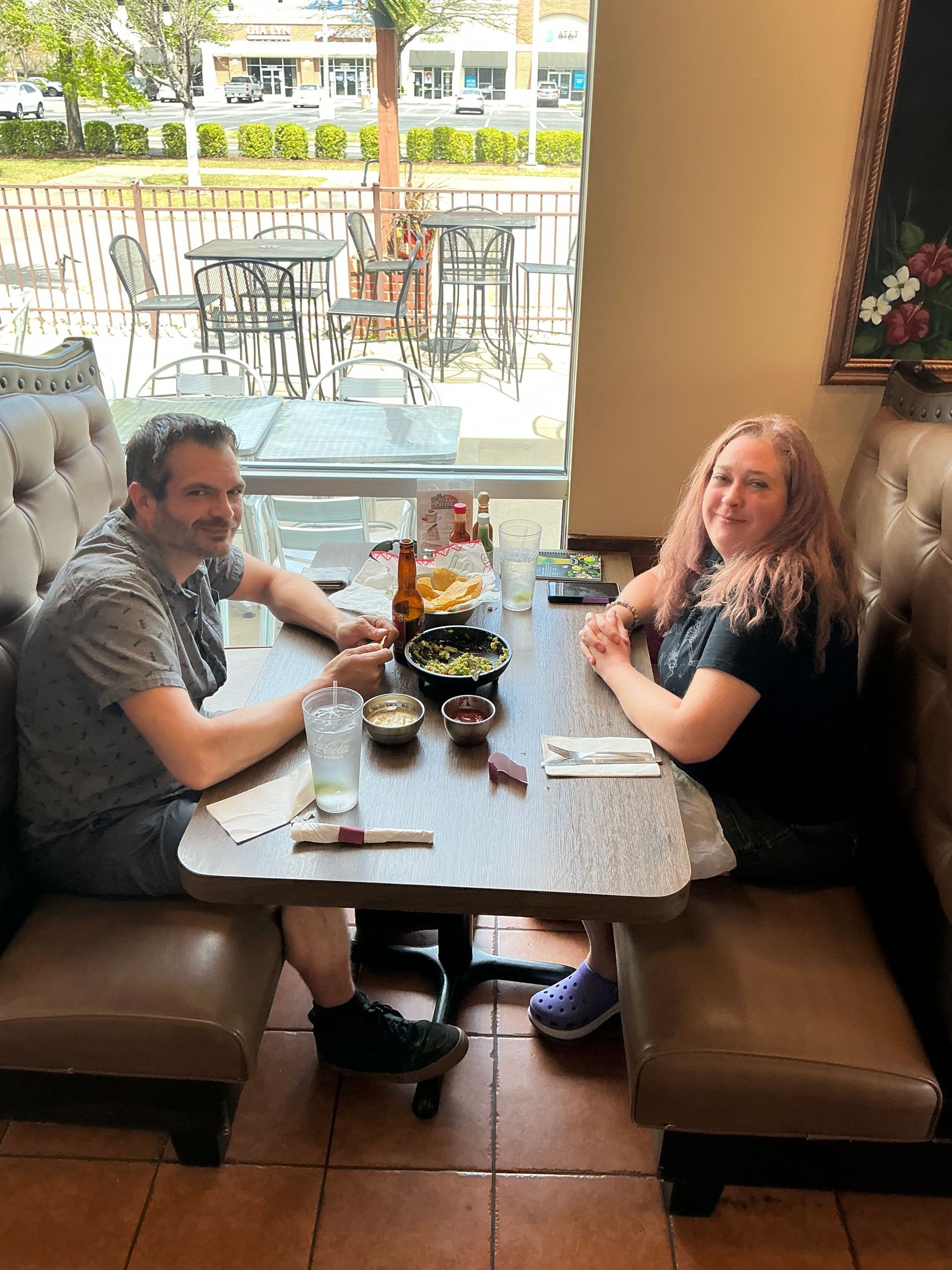 Two people sitting at a table in a restaurant near a window, enjoying a meal.