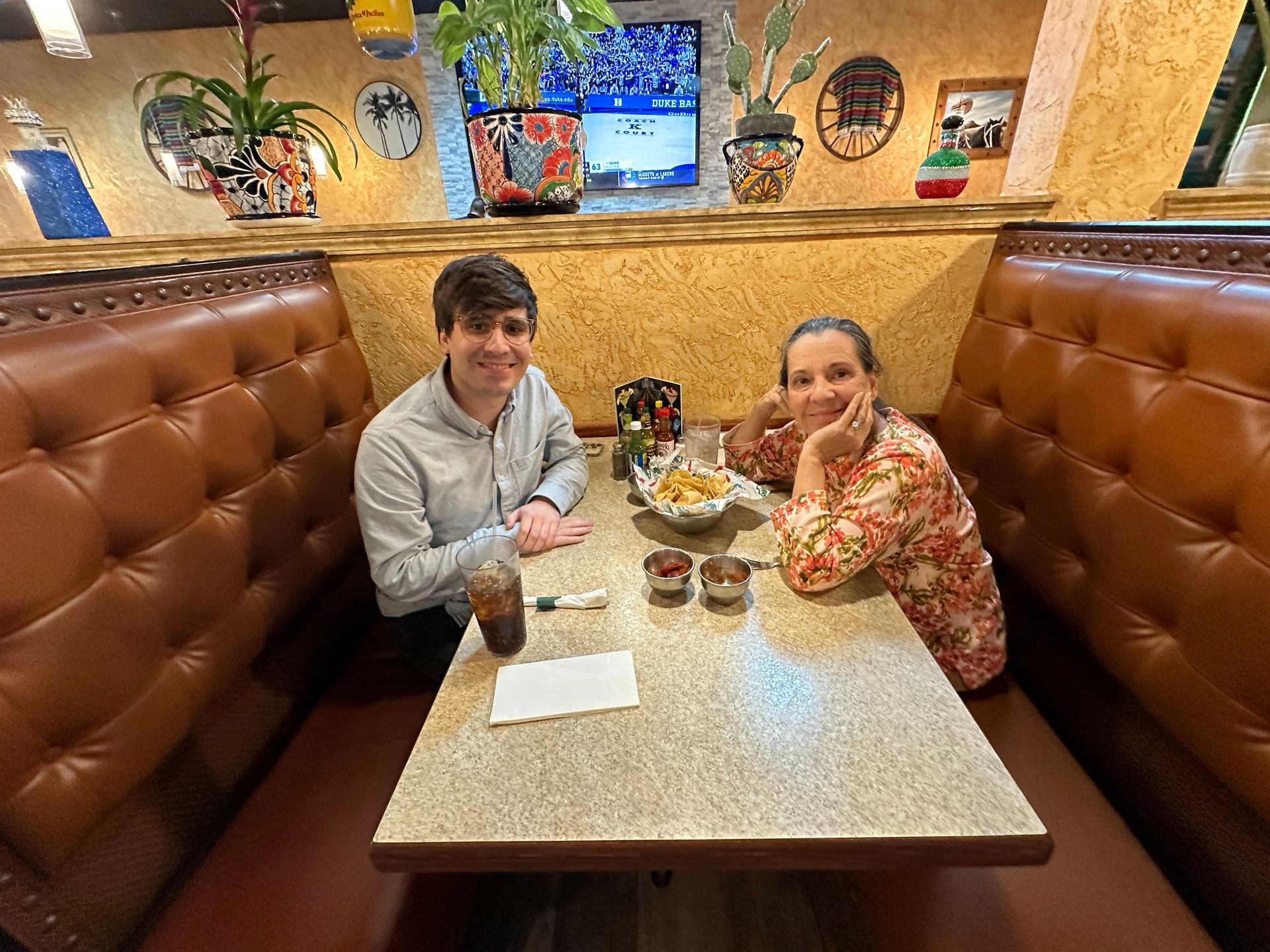 Two people sit at a table in a restaurant booth, smiling. There's a snack on the table.