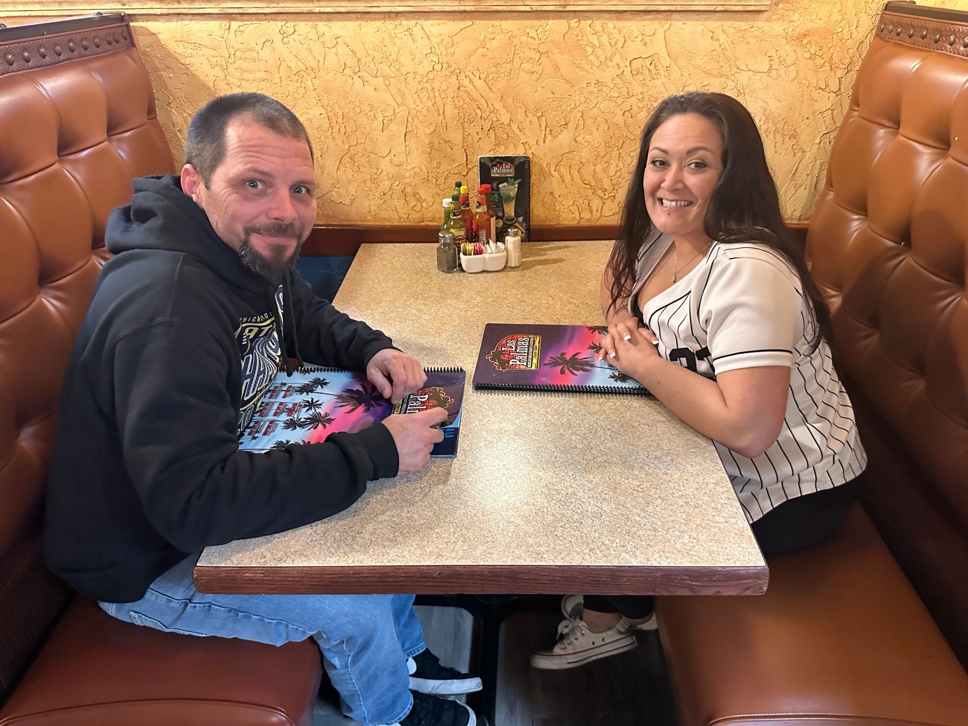 Two people seated at a booth in a restaurant, holding menus.