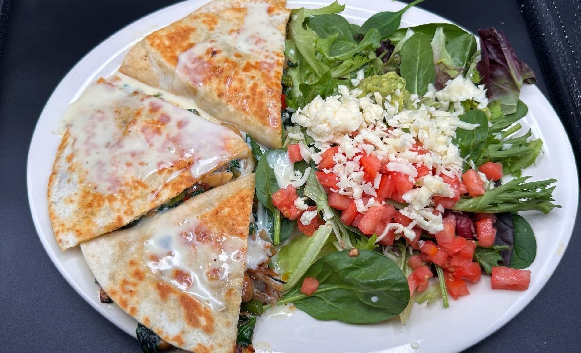 Quesadilla wedges with melted cheese, and a salad with tomatoes and cheese on a white plate.