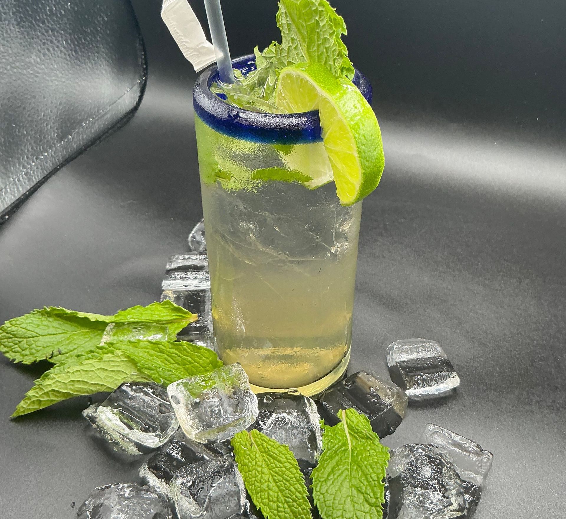 A refreshing mojito cocktail in a tall glass, garnished with lime and mint, on a black surface.