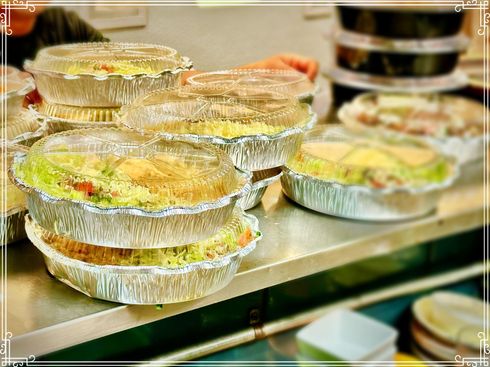 Prepared food in foil containers, stacked on a metal surface, with clear lids.