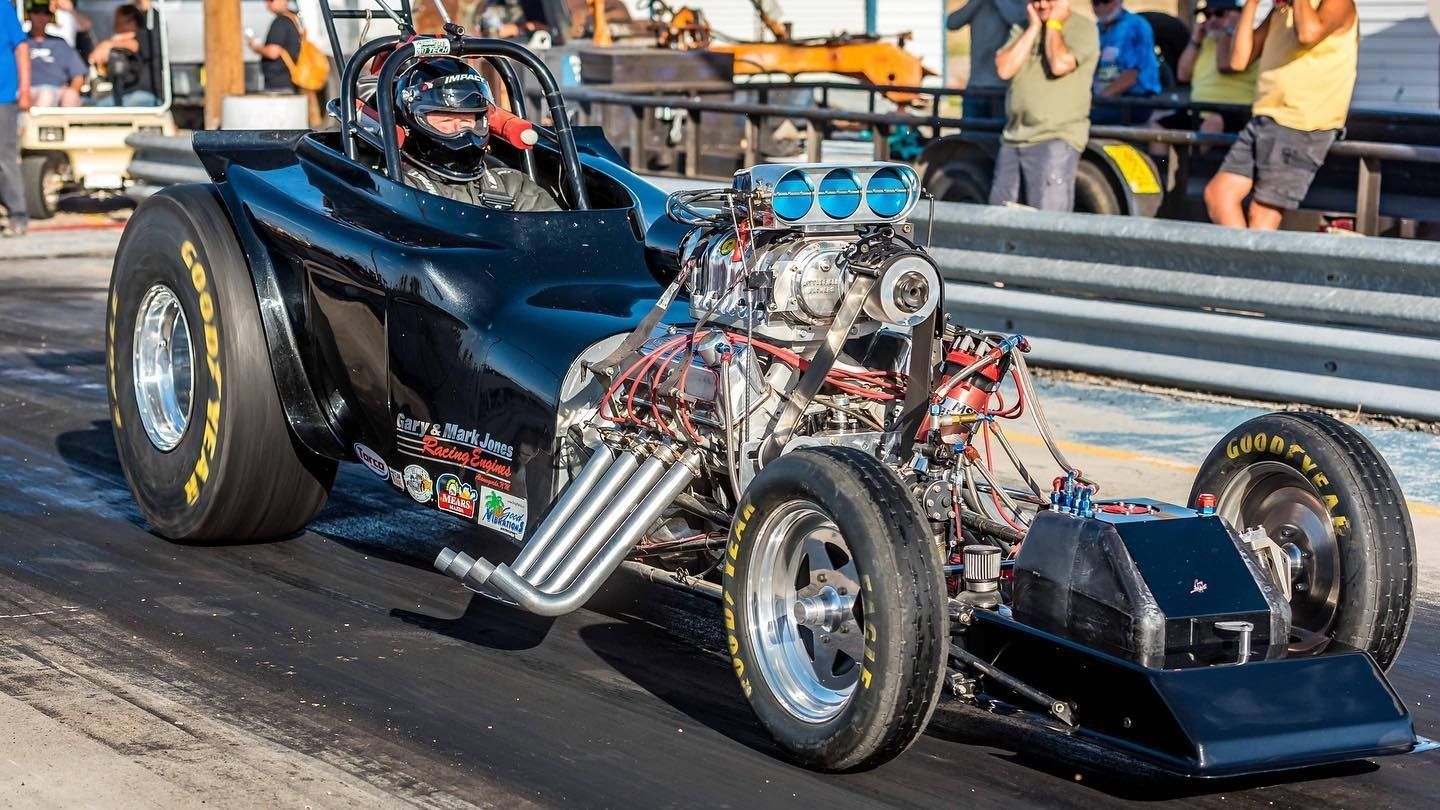 A black race car with a large engine is driving down a track.