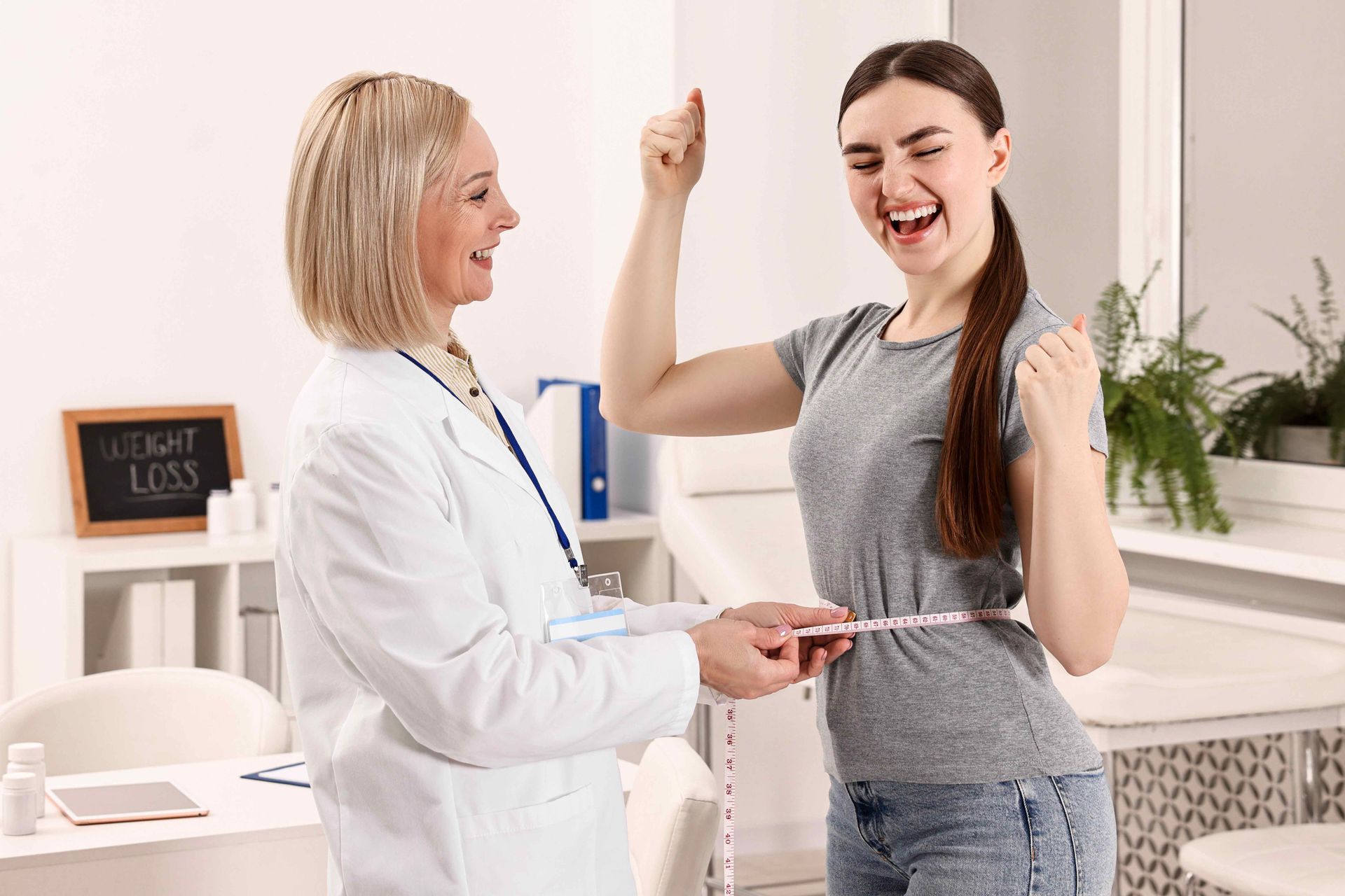 A doctor measures a patient's waist with a measuring tape. The patient celebrates with a raised fist.