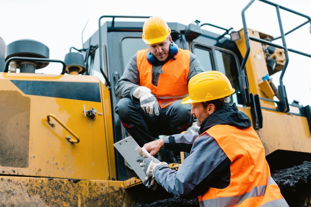 Two Construction Workers Are Sitting On A Bulldozer And Looking At A Clipboard — All Hours Vac Truck In Stanwell, QLD