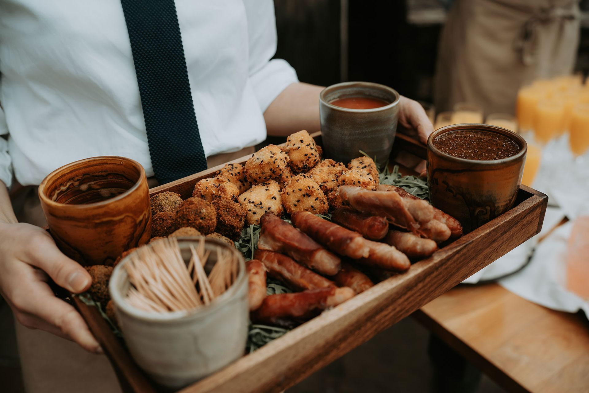 A person is holding a wooden tray filled with food and drinks.