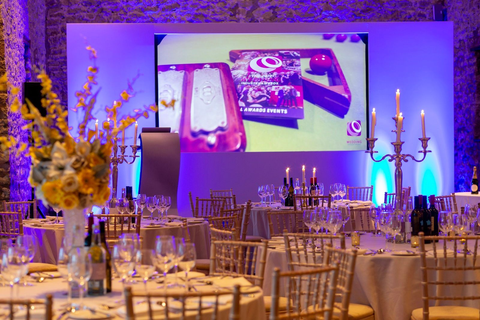 A room filled with tables and chairs and a large screen.