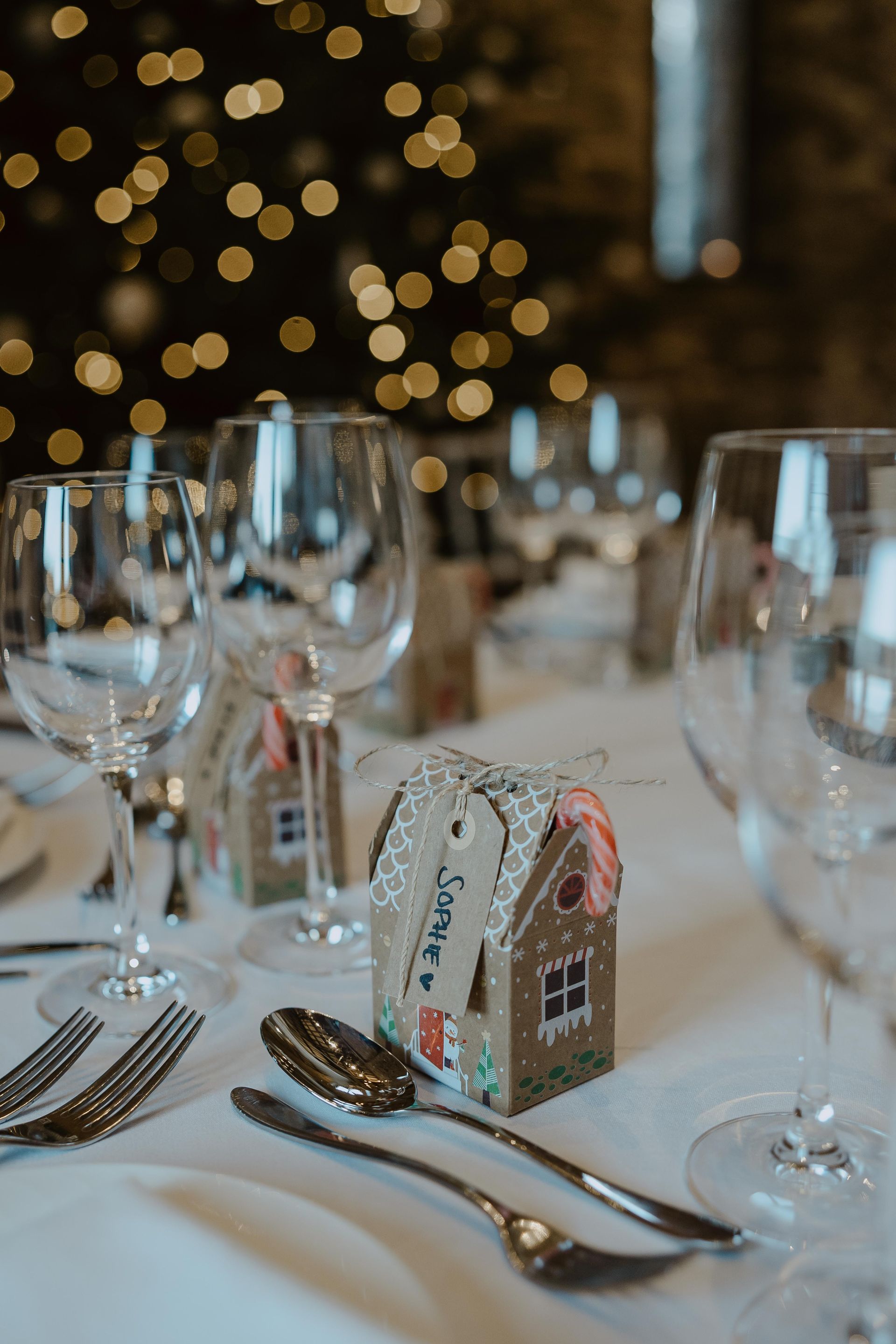 A table with glasses , silverware , and a gingerbread house on it.
