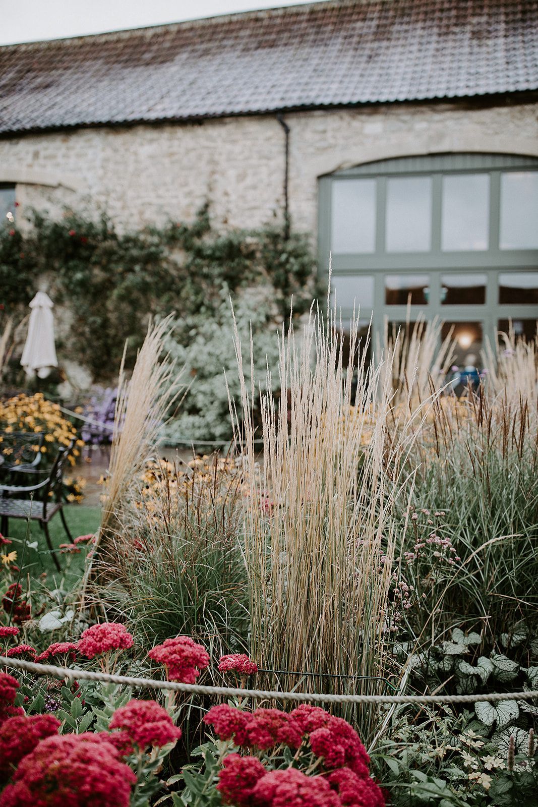 A garden with red flowers and tall grass in front of a building.