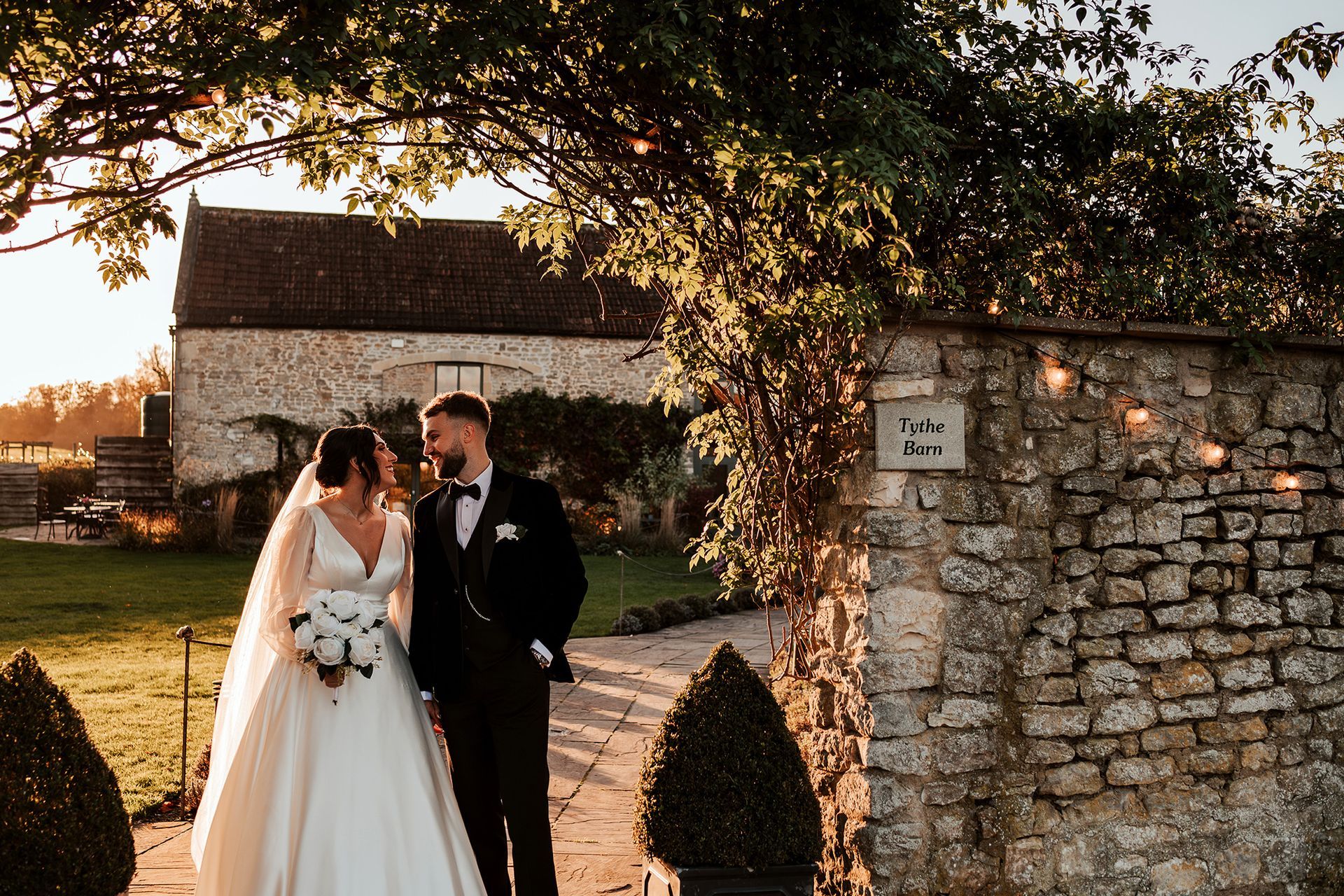 A bride and groom are standing next to each other in front of a stone wall.