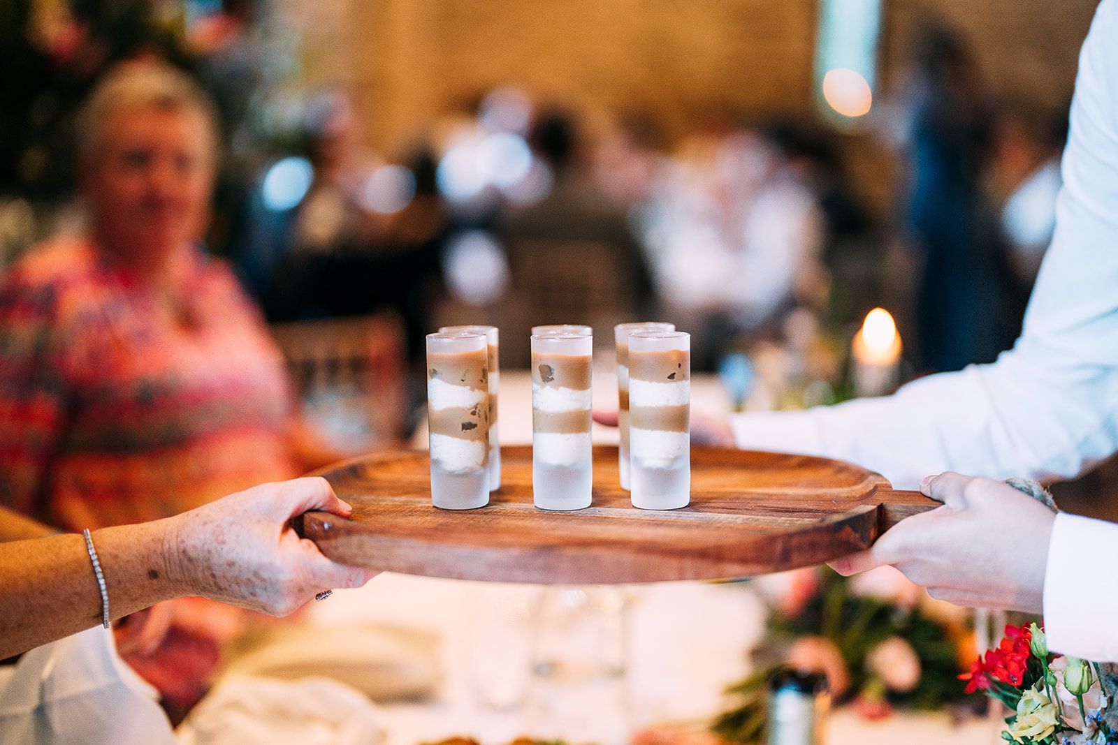 A person is holding a wooden tray with three shot glasses on it.