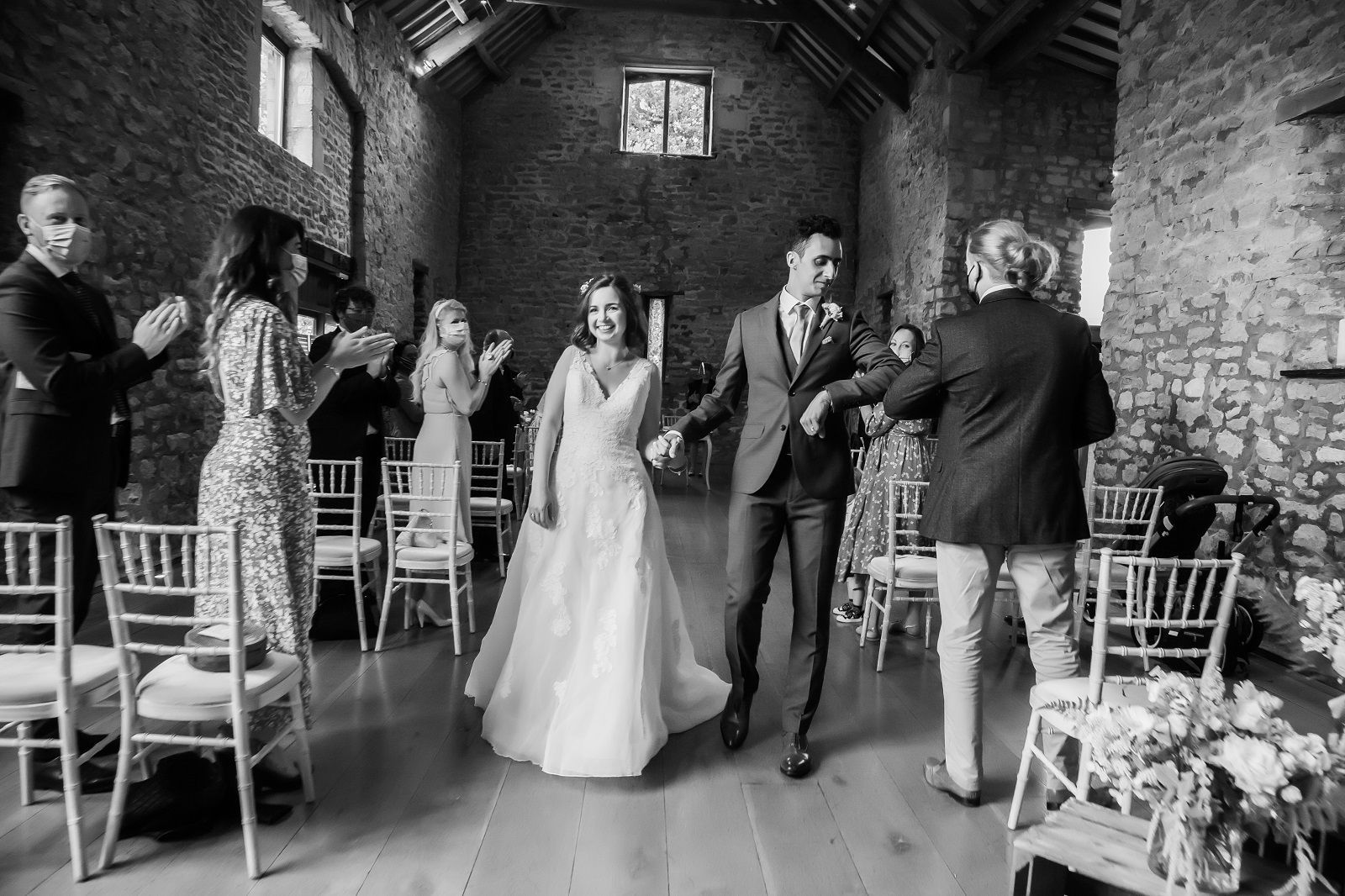 A black and white photo of a bride and groom walking down the aisle at their wedding.