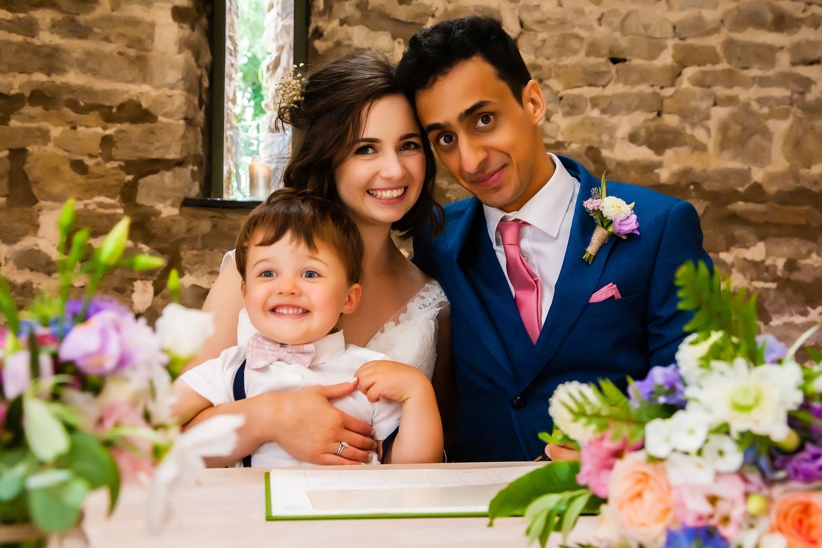 A bride and groom are posing for a picture with their son at their wedding.