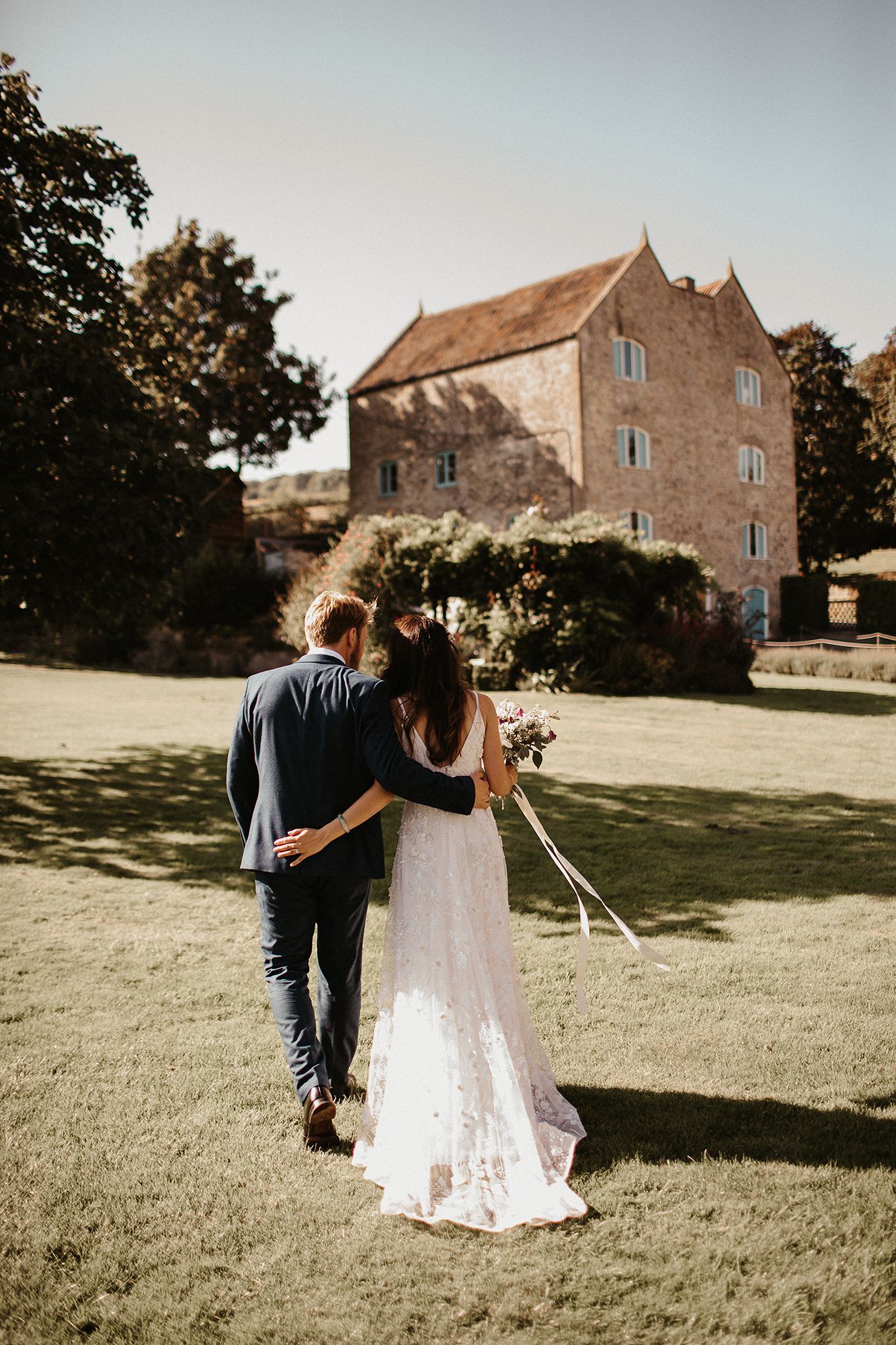 A bride and groom are walking in a field in front of a large building.