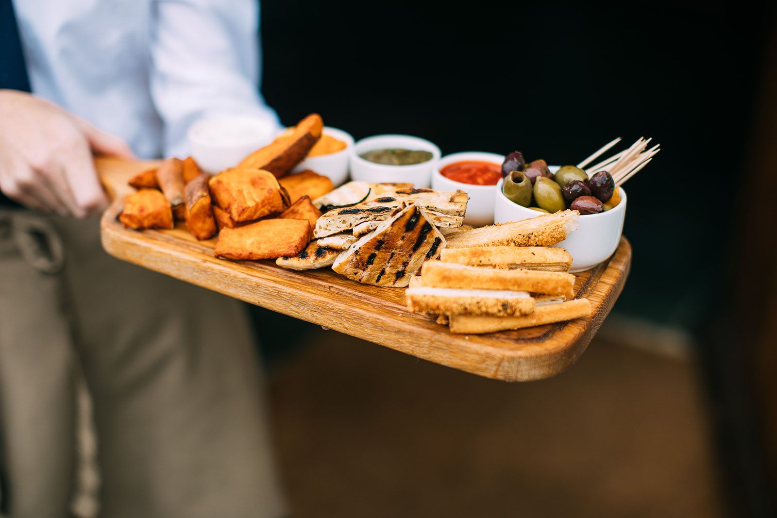 A person is holding a wooden tray with a variety of food on it.