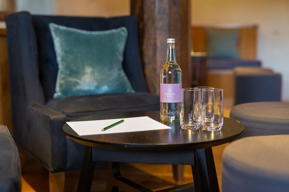A chair is sitting next to a table with a bottle of water and glasses on it.