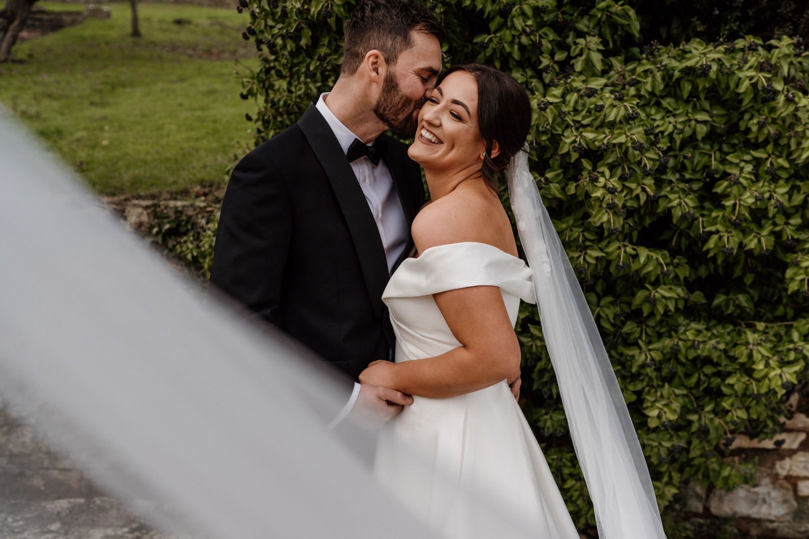 A bride and groom are posing for a picture with a veil blowing in the wind.