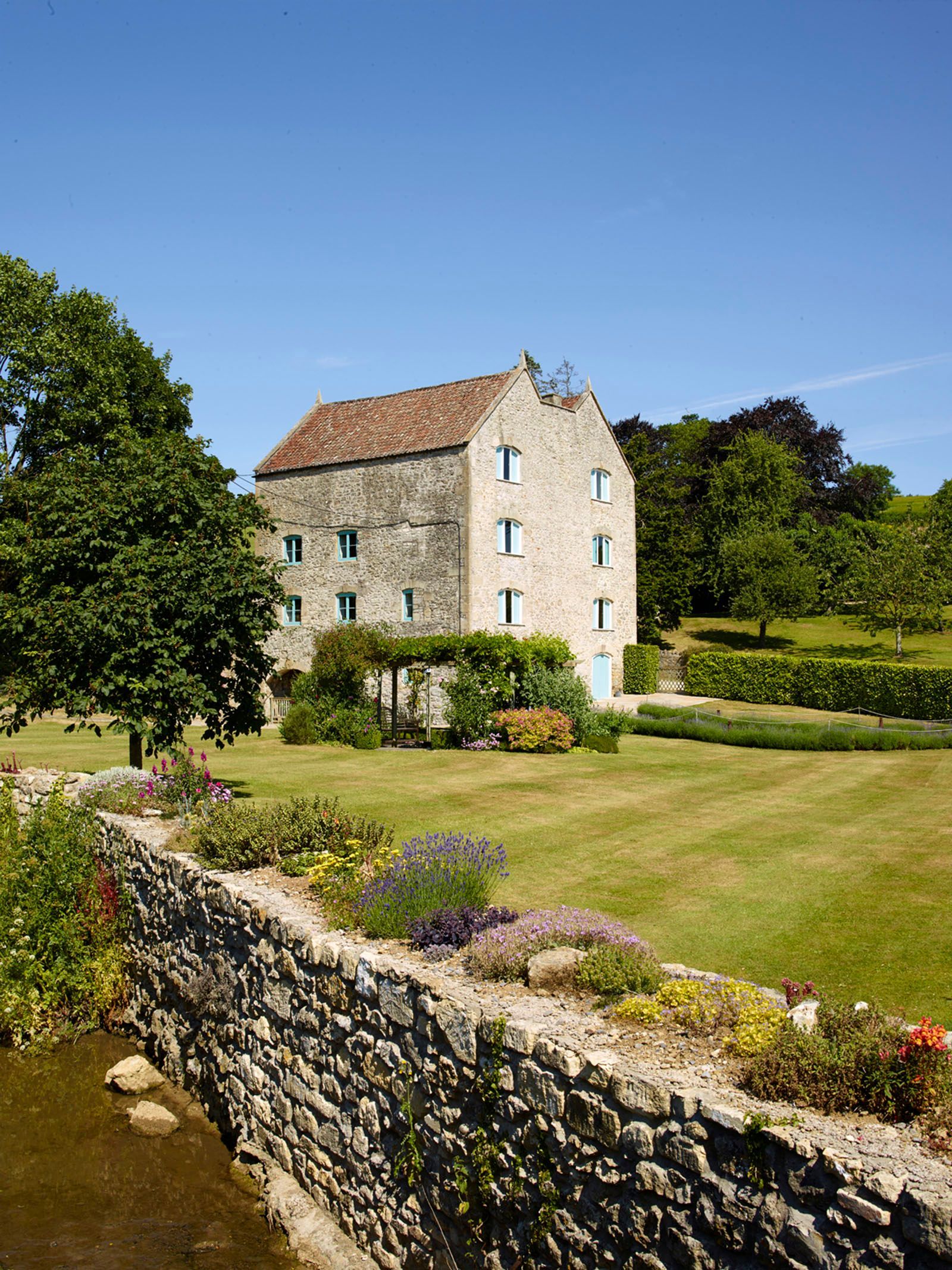 A large stone building is sitting in the middle of a lush green field next to a stone wall.
