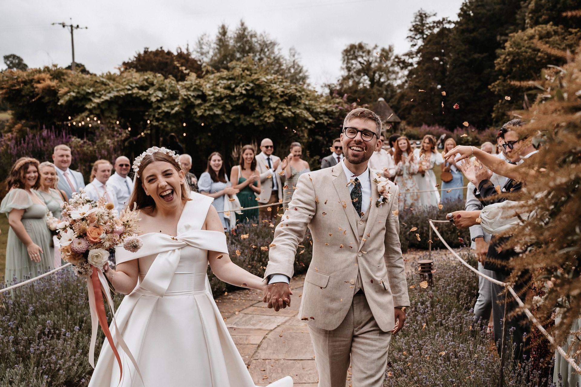 A bride and groom are walking down a path holding hands.