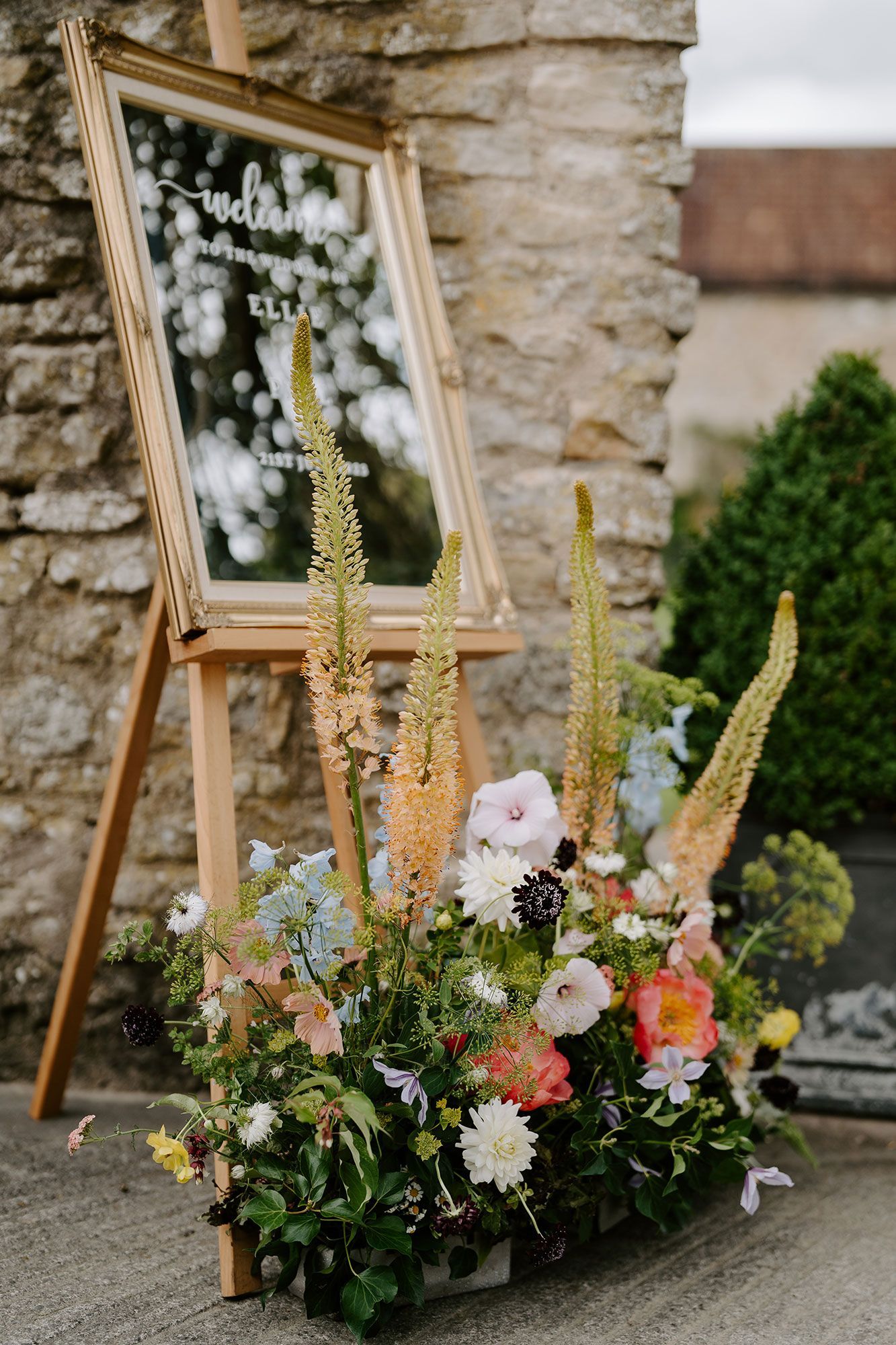 A large mirror sitting on top of a wooden easel surrounded by flowers.